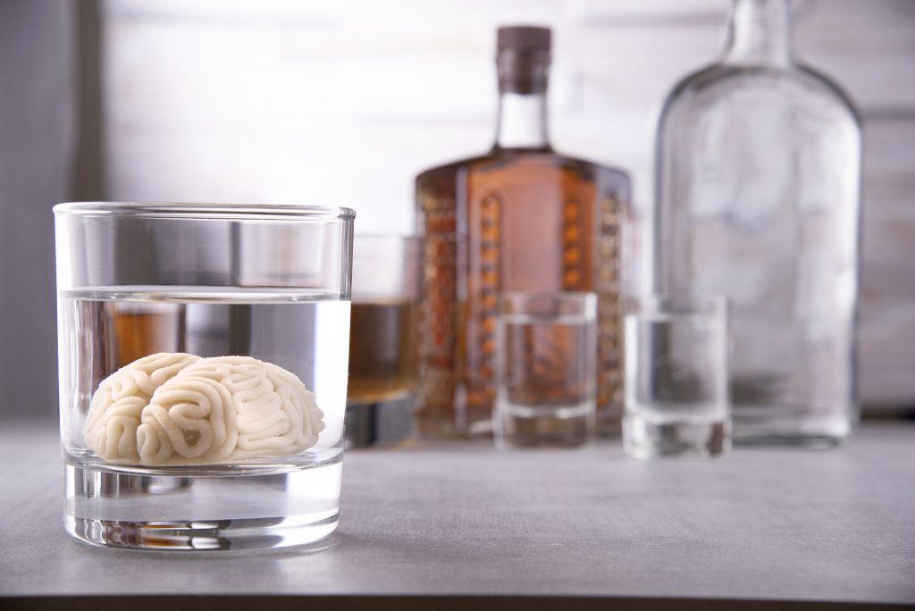 human brain in a glass with an alcoholic drink, against the background of bottles with alcohol. Alcohol addiction. Harm to the brain from alcohol