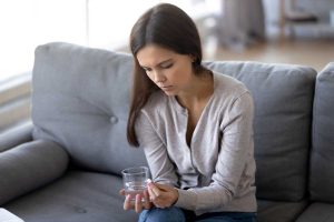 girl holding pill and glass of fresh water, taking medicine
