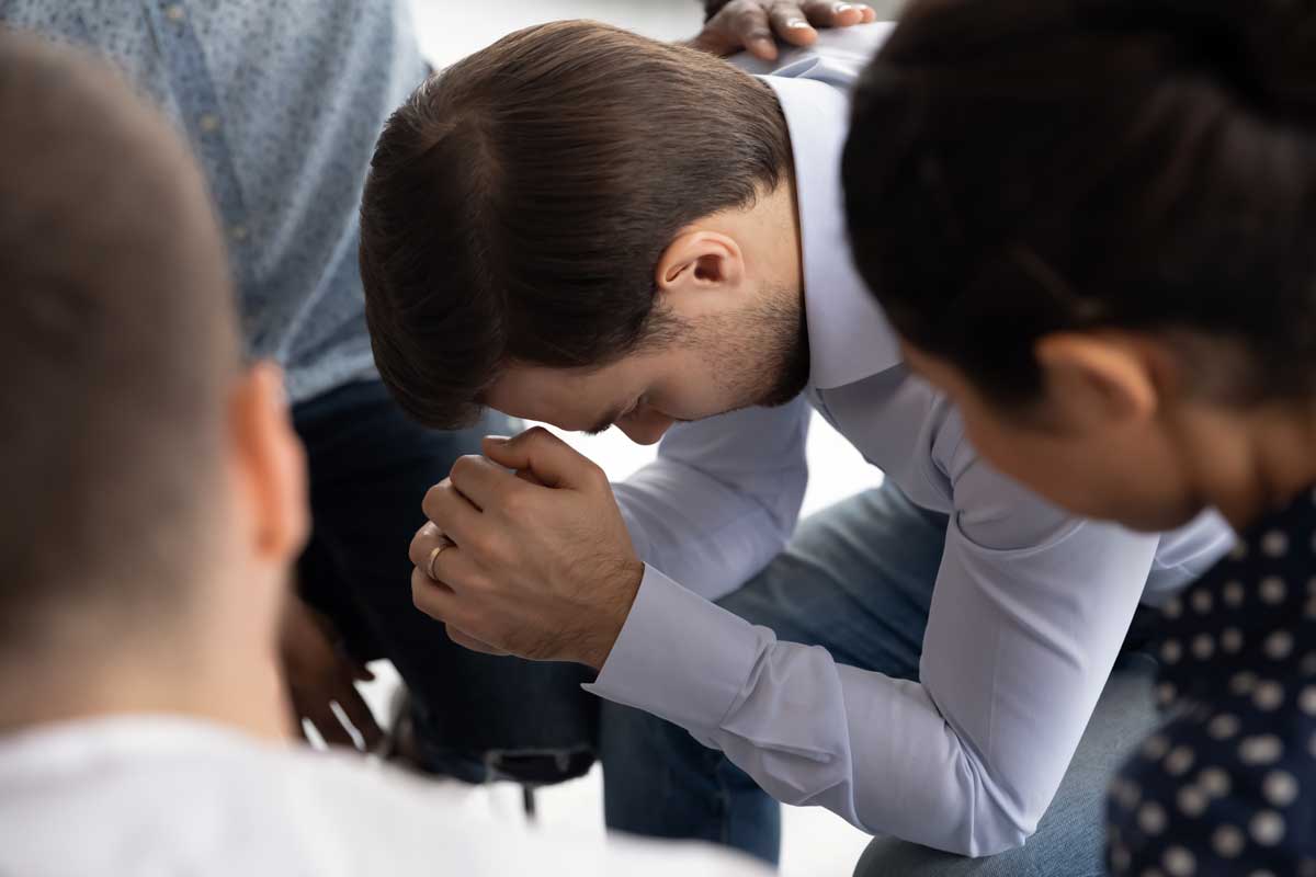 Close up of stressed young man feel anxious frustrated participate in group psychological therapy, diverse young people help comfort depressed male patient at psychotherapy counseling session